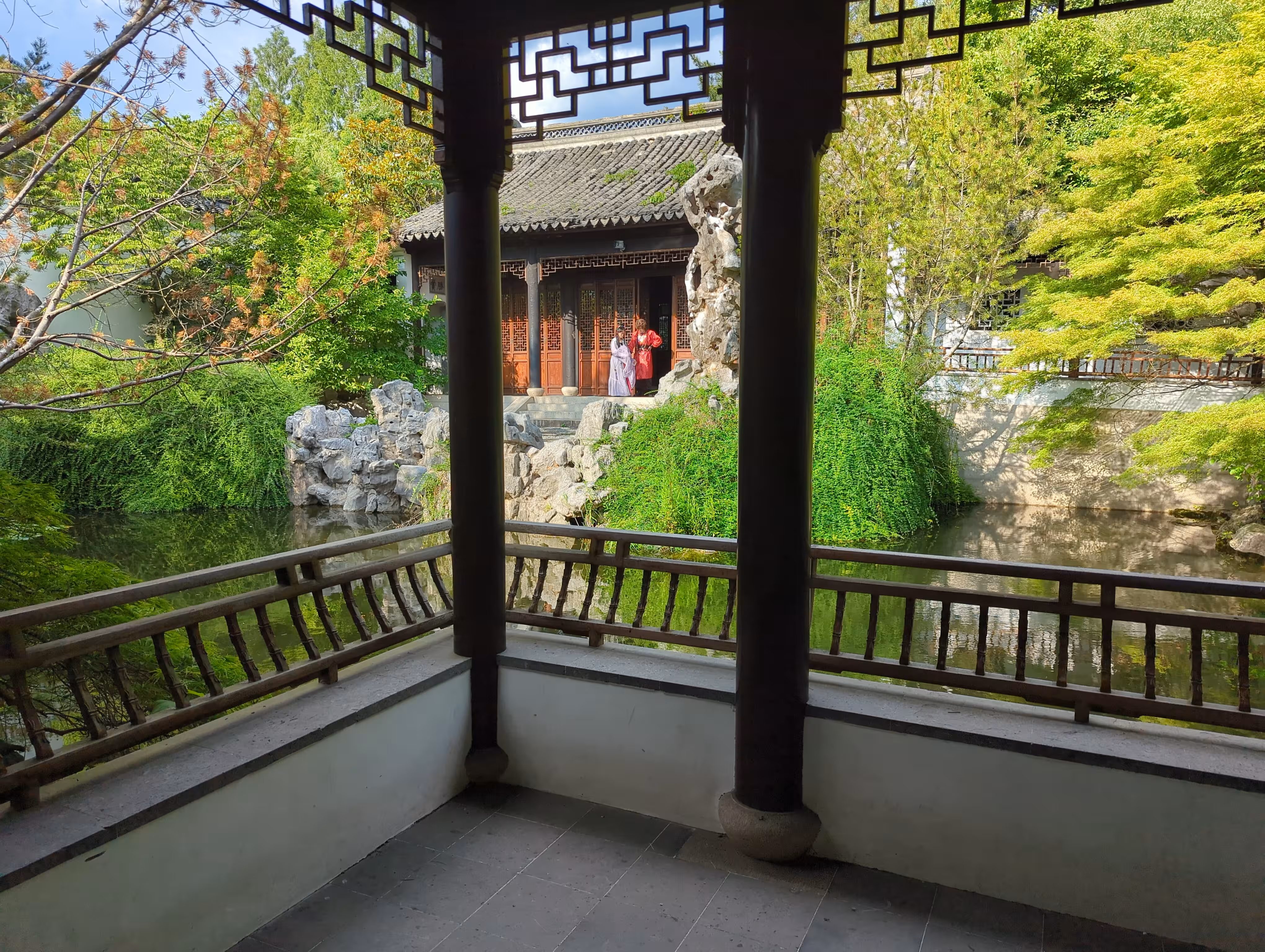 A Chinese garden with a pond and two people in pseudo-traditional costumes